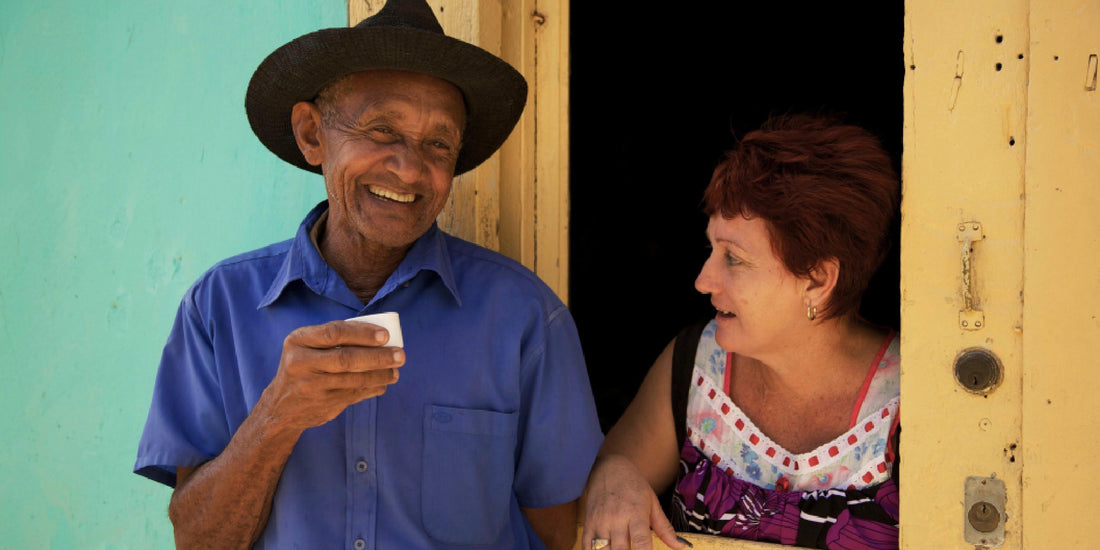 A woman talks through the window to a Cuban man drinking coffee on the street outside