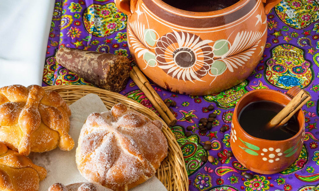 Coffee in old style Latin American pots, placed on a tablecloth with a Mexican skull pattern, next to a plate of pastries
