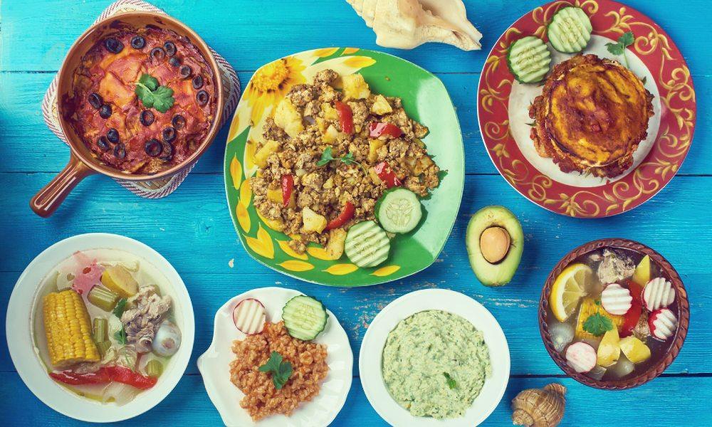Birdseye shot of a blue table containing Mexican dishes: corn, chile con carne, salads, avocado and beans