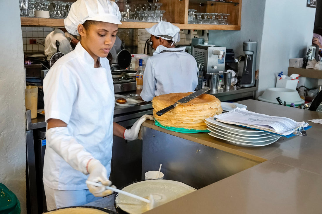 Chef at Crepes & Waffles, in white overalls, making a giant crepe in an open kitchen