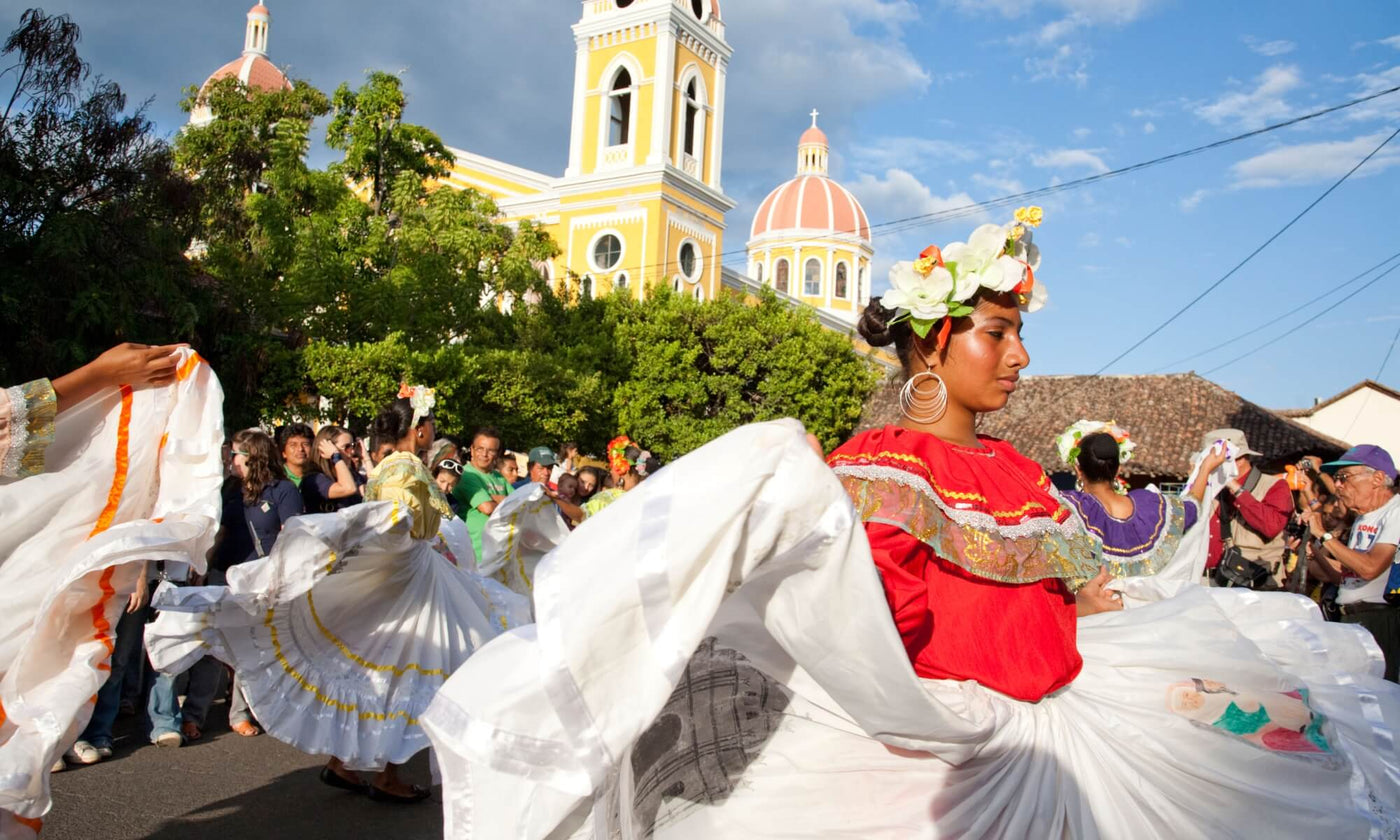 Women wearing floral headdresses and white skirts dance in the square as part of a festival in Nicaragua