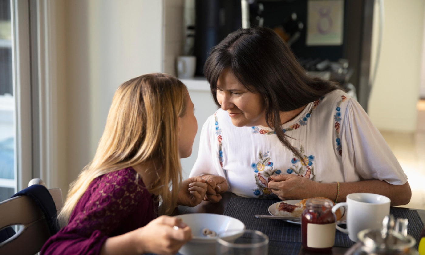 A mother and daughter eat breakfast and drink coffee at the dining table