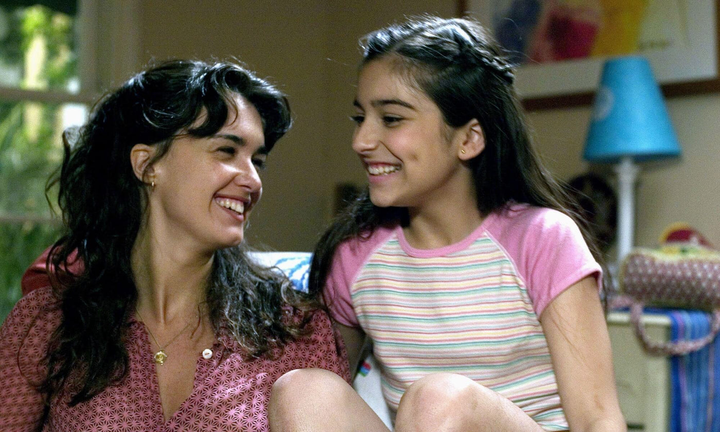 A Latina woman and her daughter laughing, sat on their sofa in the front room