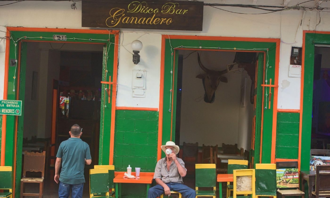 A man sits on the street, drinking coffee outside a colonial building in Colombia