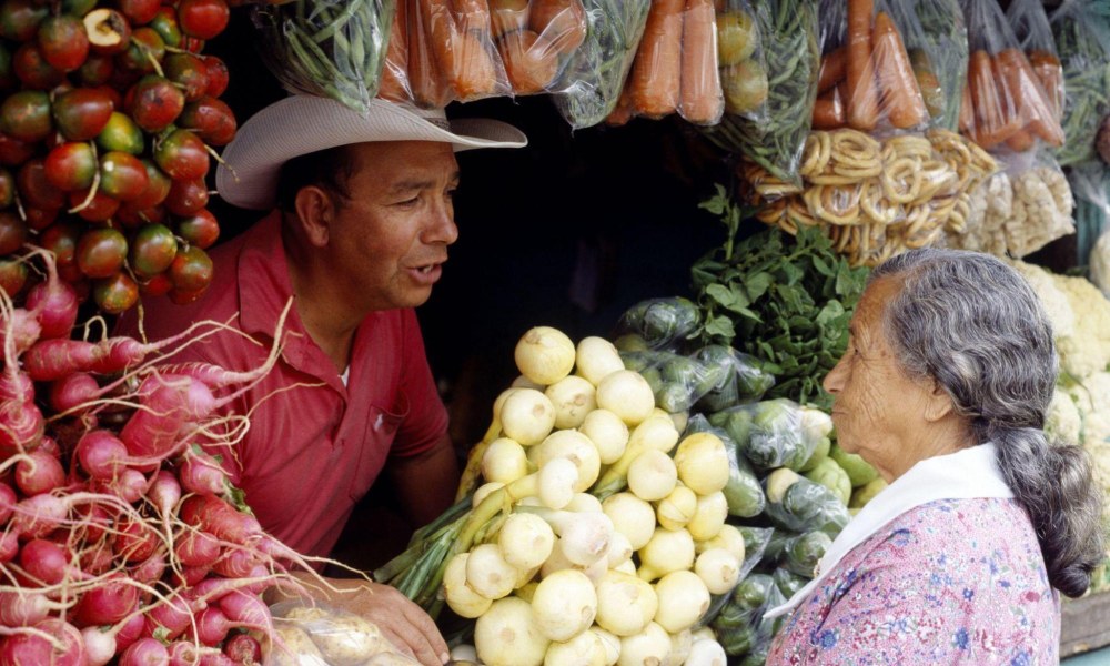 a male vendor at a vegetable stall in Nicoya chatting amiably with a centenarian Nicoyan lady