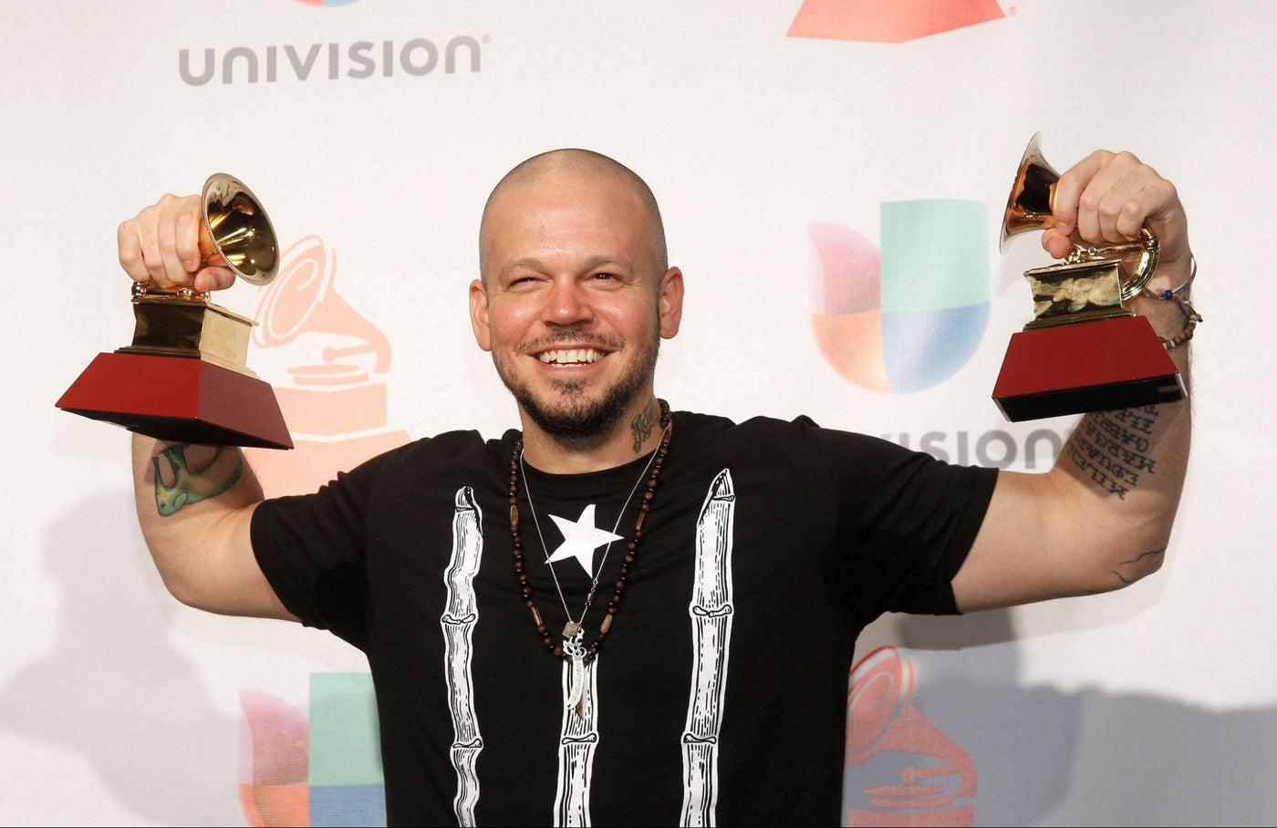 Puerto Rican rapper, Resident, holding a Latin Grammy Award in each hand
