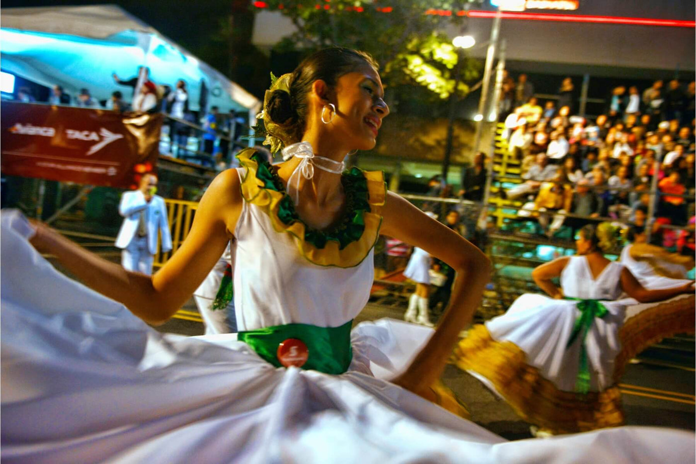 Latin American woman wearing a white dress with green embellishments, dancing as part of a show