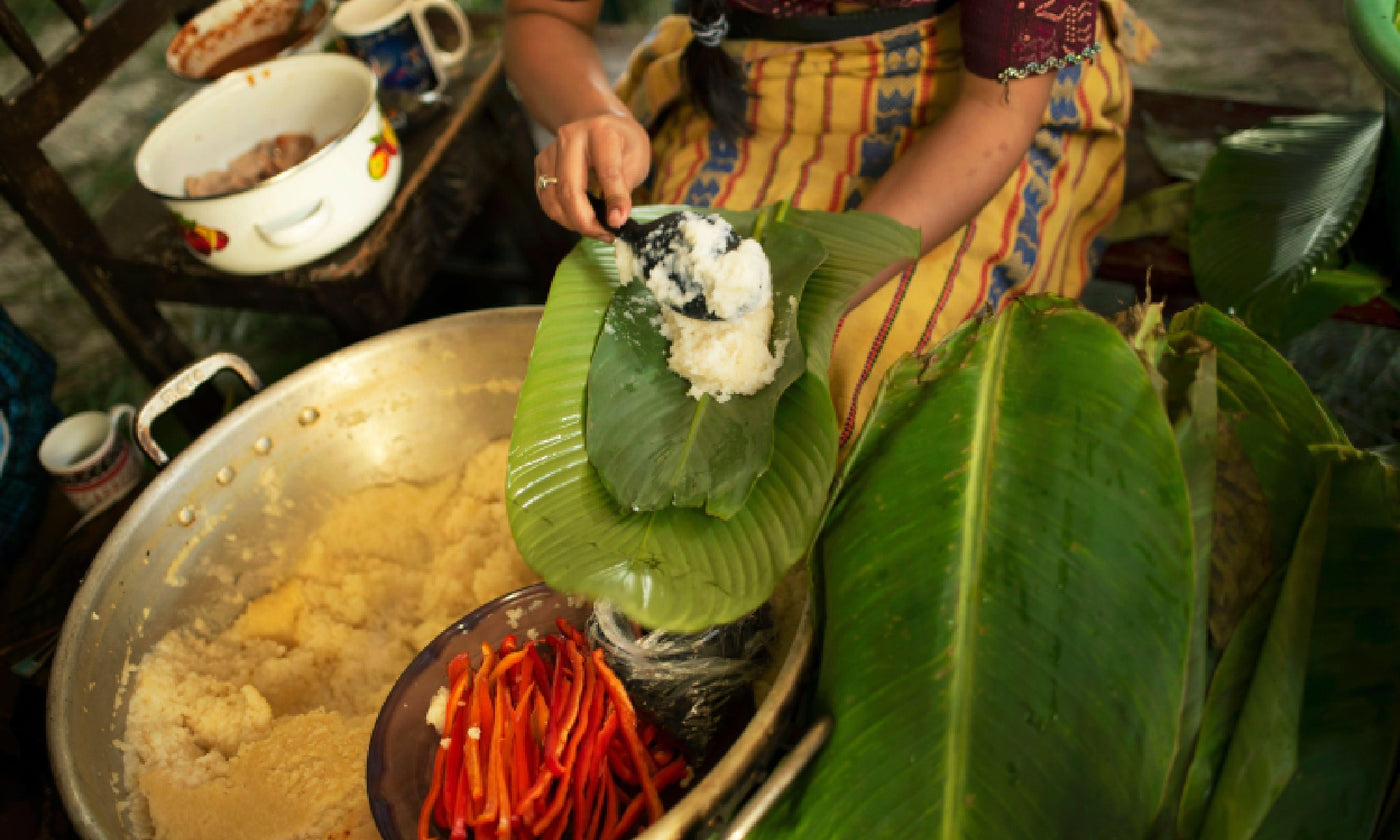 A woman puts tamale flour mixture into a banana leaf