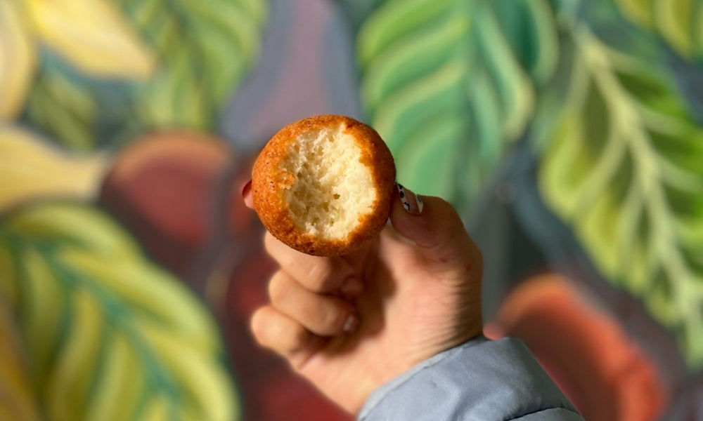 Hand holding a half-bitten pan de elote in the shape of a round ball