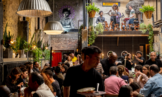 the inside of a busy, colonial-style restaurant, waiter in foreground and a live band playing 