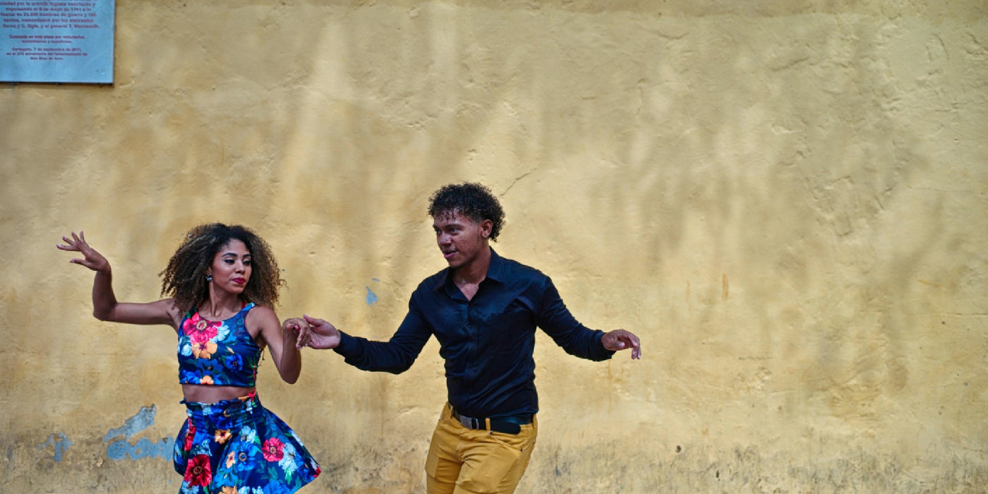 Couple dance salsa in front of a colonial, yellow wall of a building