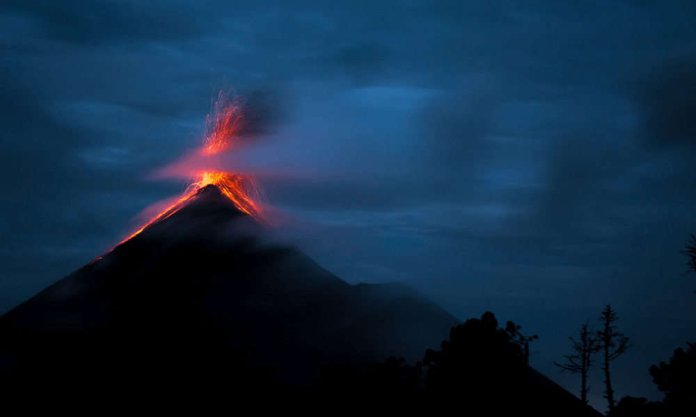 A volcano erupting lava and ash into the night sky