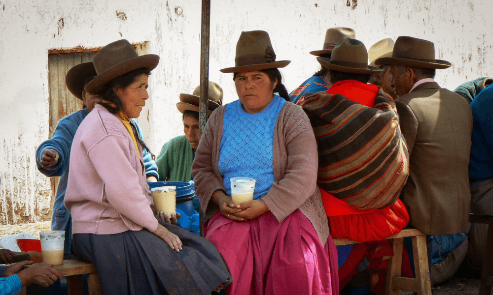 Women in indigenous clothing and bowling hats drink chicha in a street in Latin America