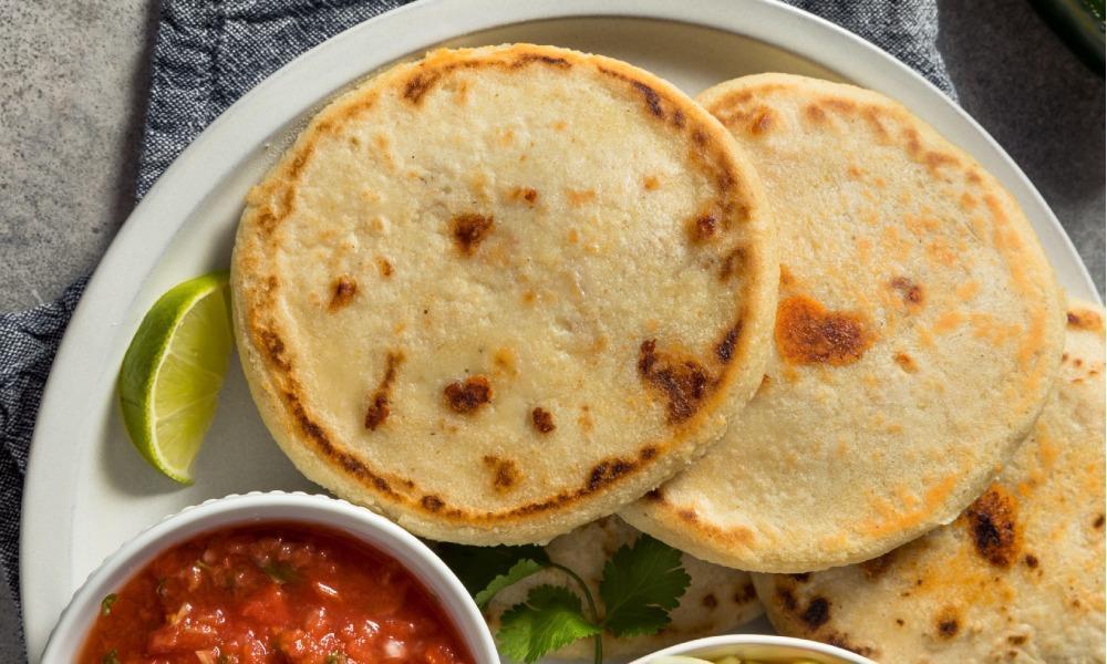 3 pupusas on a plate with a small bowl of red salsa